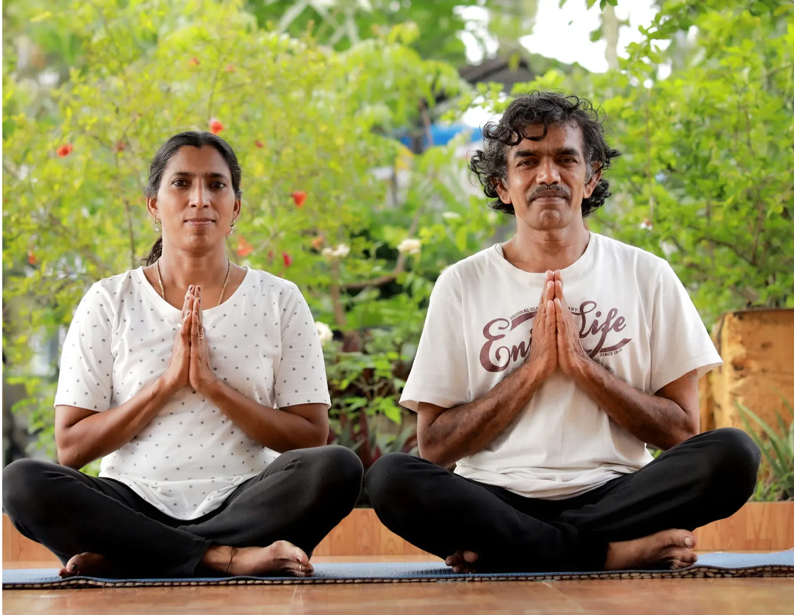 Ayurtheeram founders Anitha and Ramesh seated cross-legged in meditation with hands in namaste
